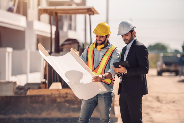 Engenheiro civil e gerente de construção civil segurando tablet digital e as plantas da obra em que estão
