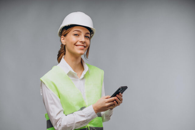 Mulher de negócios da construção usando colete e capacete falando ao telefone