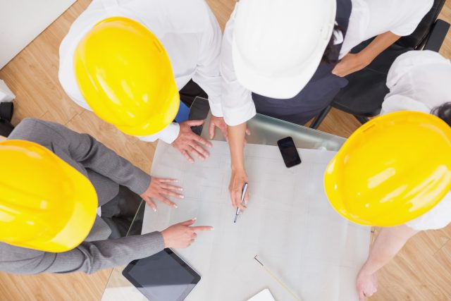 Imagem superior de trabalhadores da construção civil olhando uma mesa com vários papéis