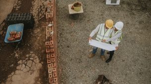 Foto de dois homens em um canteiro de obras olhando um projeto no papel. Vista de cima.