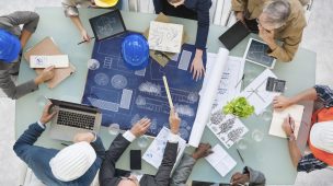 Visão de cima de uma mesa com um grupo de pessoas sentados em volta planejando obra