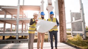 Imagem de 3 pessoas com IPIs de construção analisando a planta de uma obra