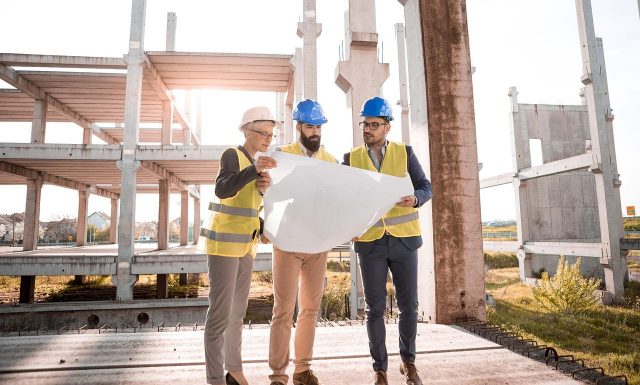 Imagem de 3 pessoas com IPIs de construção analisando a planta de uma obra