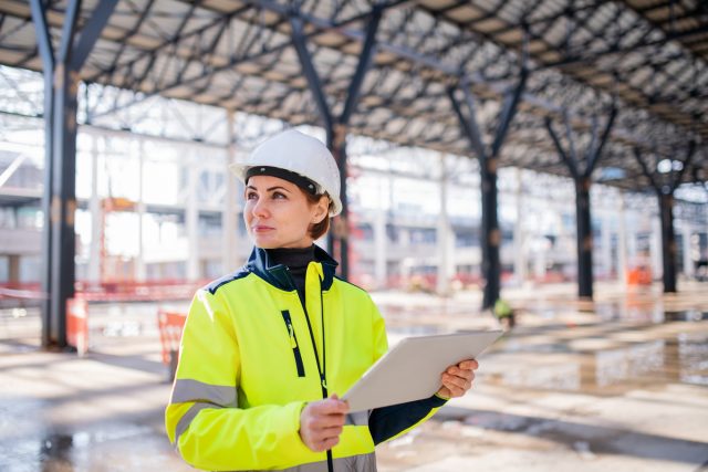 Uma mulher engenheira com tablet em pé no canteiro de obras, trabalhando.