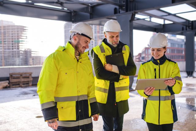 Grupo de engenheiros de pé ao ar livre no canteiro de obras, usando tablet