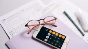 mesa com papeis, óculos, celular com a calculadora na tela