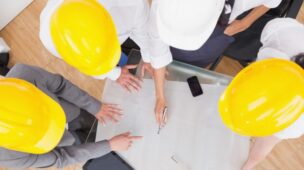 Equipe com capacetes analisando planta em reunião de planejamento com uso de sistema de gestão de obras.