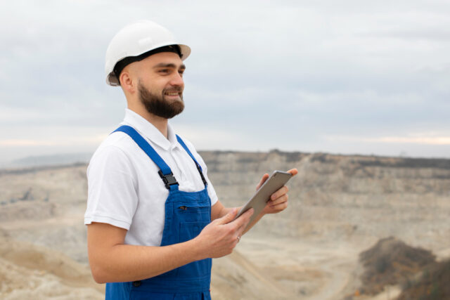 Homem que trabalha na construção civil segurando um tablet para preencher o relatório de auditoria interna